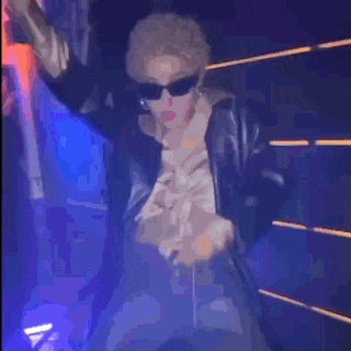 a woman wearing sunglasses and a fur coat is standing in a dark room .