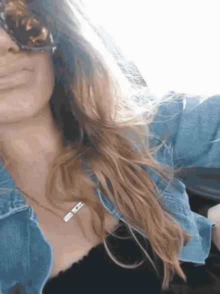 a woman wearing sunglasses and a denim jacket has a necklace around her neck with the letter b on it