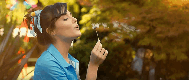 a woman blowing a dandelion in the air