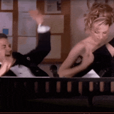 a man in a tuxedo is laughing while a woman in a black dress stands behind him