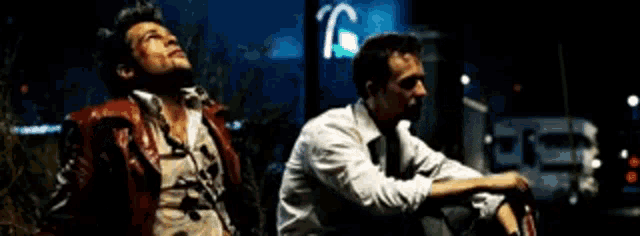 two men are sitting next to each other in a dark room looking up .