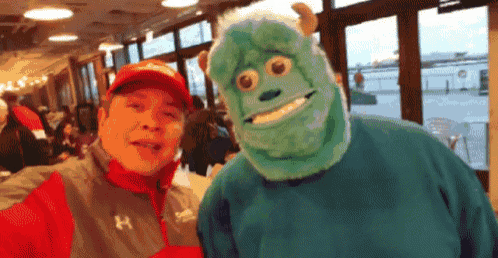 a man in a red hat is standing next to a man wearing a sully mask