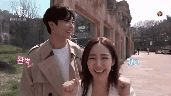 a man and a woman are holding hands and smiling in front of a building with foreign writing