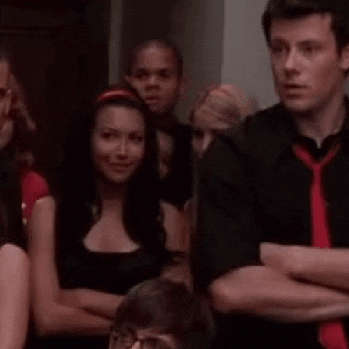 a man in a black shirt and red tie is sitting in a crowd of people