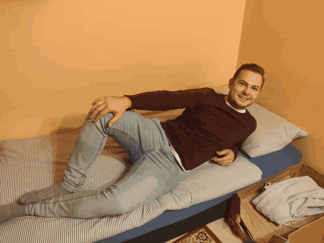 a man laying on a bed with his legs crossed and a cardboard box next to him