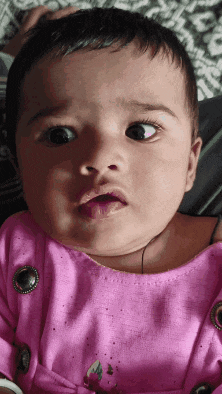 a baby girl in a pink dress is making a funny face .