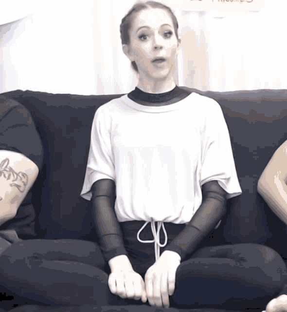 a woman sits on a couch with a tattoo on her arm that says ' a ' on it