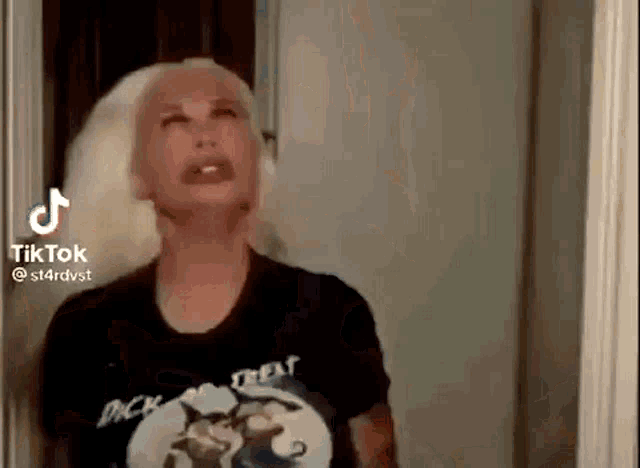 a woman with blonde hair is wearing a black t-shirt and making a funny face .