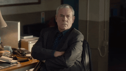 a man in a suit and tie sits with his arms crossed