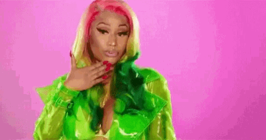 a woman with green and red hair is wearing a green jacket and standing on a pink background .