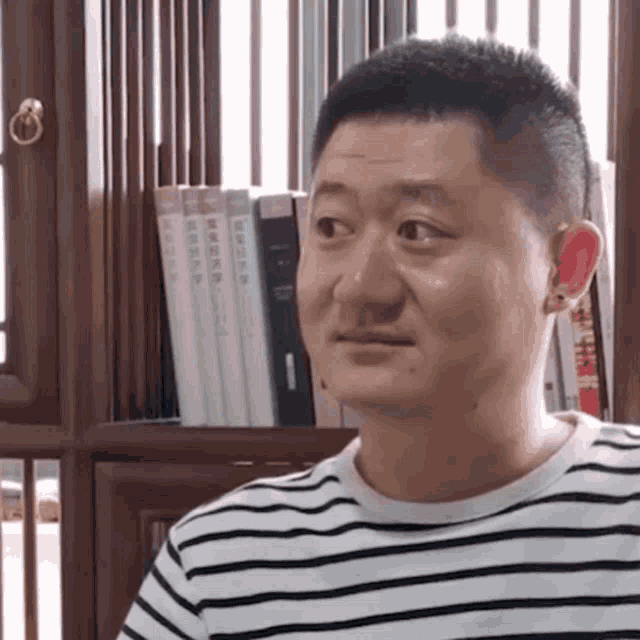 a man in a striped shirt is sitting in front of a book shelf .