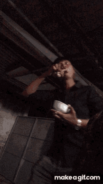 a man in a black shirt is eating something from a bowl with a spoon