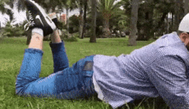 a man is laying on his stomach in the grass with his feet up .