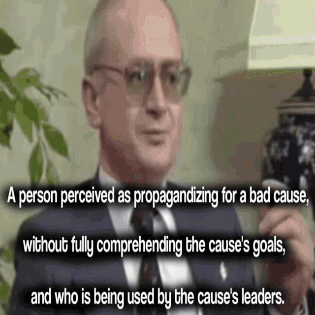 a man wearing glasses and a suit is talking about a person perceived as propagandizing for a bad cause