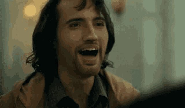 a man with long hair is laughing with his mouth open in a close up of his face .
