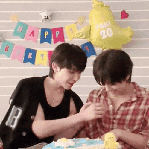 two men are sitting at a table with a cake and balloons .