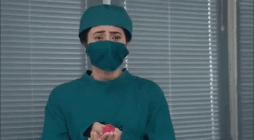 a female surgeon wearing a mask and surgical gown is holding a red object .