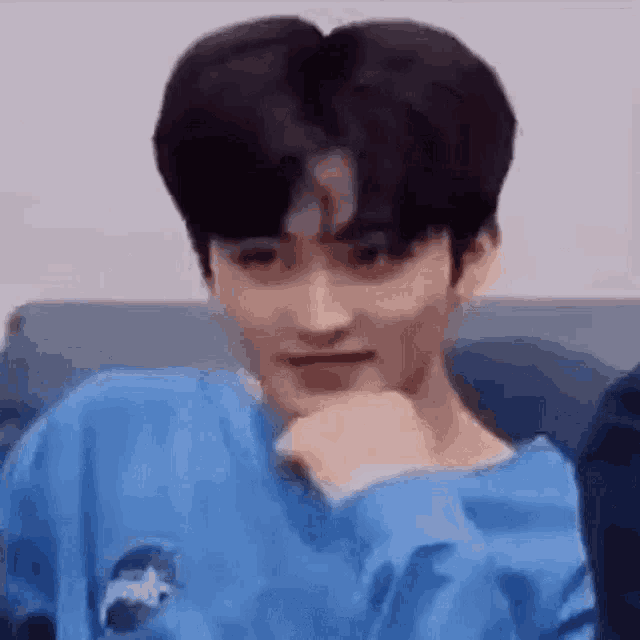 a young man in a blue sweater is sitting on a couch and making a funny face .