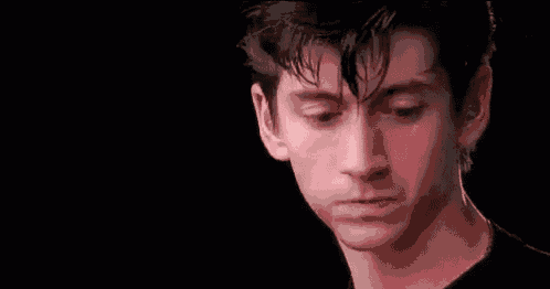 a close up of a young man 's face with a black background and ear buds in his ears .