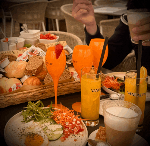 a table full of food and drinks including a glass of orange juice that says vanilia