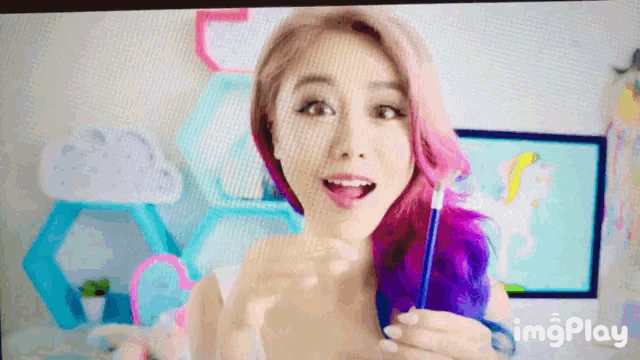 a woman with pink and purple hair is holding a pen in front of a computer screen which says imgplay