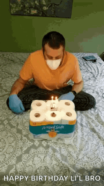 a man wearing a mask and gloves is sitting on a bed with a birthday cake made out of toilet paper