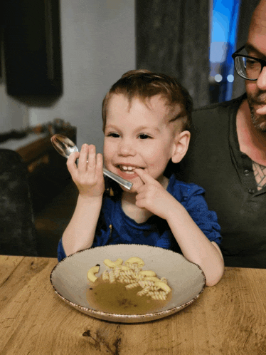 a little boy is eating macaroni and cheese with a spoon from a bowl