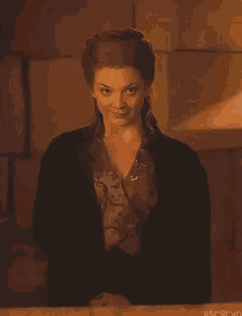 a woman in a black jacket is standing in front of a wooden wall .