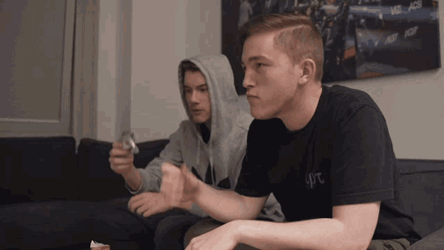 two young men are sitting on a couch playing a video game and one of them has a shirt that says 4rt on it