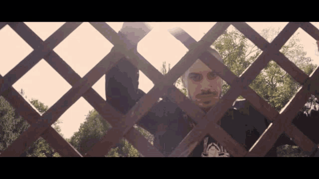 a man behind a wooden fence with a shirt that says ' a ' on it
