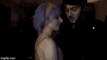 a woman with purple hair is dancing with a man in a dark room ..