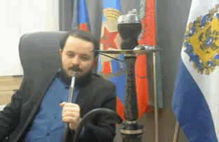 a man in a suit is smoking a hookah in front of flags .