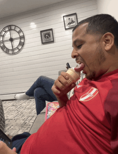 a man in a red shirt is eating an ice cream cone with his tongue out