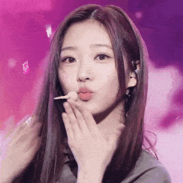 a woman with long hair is blowing a kiss with a lollipop in her mouth .