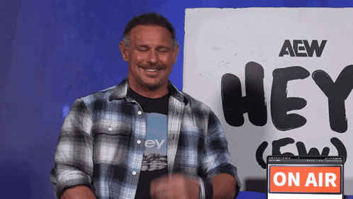 a man stands in front of a sign that says aew hey