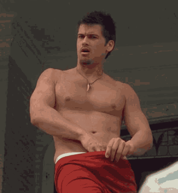 a shirtless man wearing red shorts and a necklace