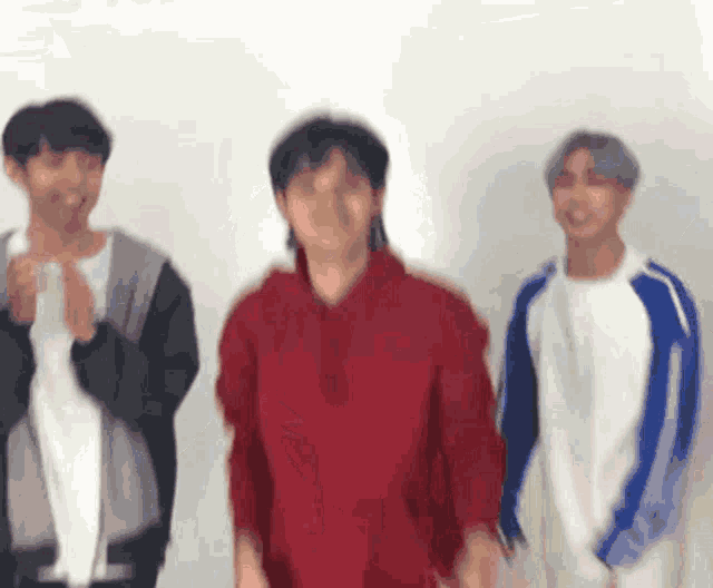 three young men are standing next to each other and one of them is wearing a red hoodie