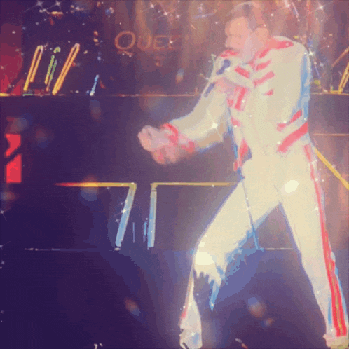 a man singing into a microphone with queen in the background