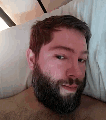 a man with a beard and mustache is laying in bed with a pillow .