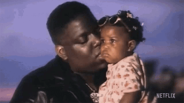 a man is kissing a little girl on the cheek while holding her in his arms .