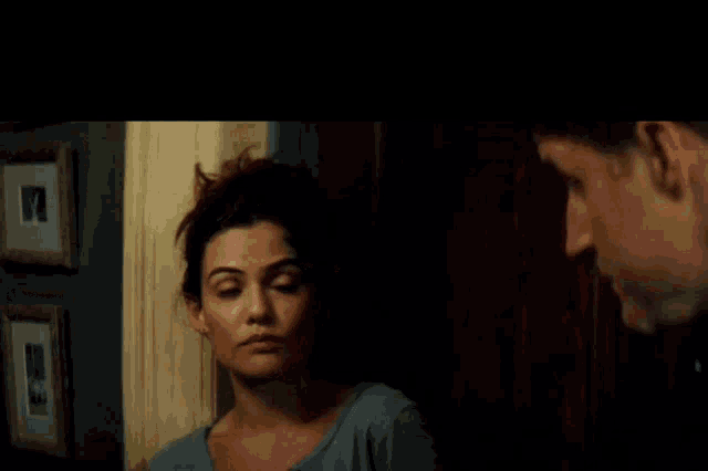 a man and a woman are looking at each other in a dark room with pictures on the wall