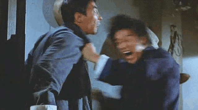 two men are fighting in a room and one of them is laughing .