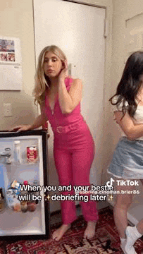 a woman in a pink jumpsuit is standing in front of a mini refrigerator .