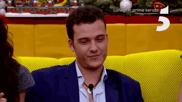 a man in a suit is sitting on a yellow couch with a sign that says luned in prima serata