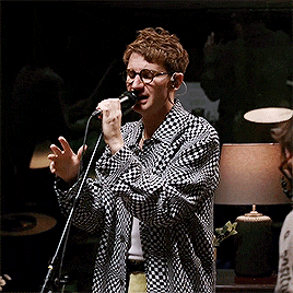 a man singing into a microphone wearing glasses and a plaid shirt
