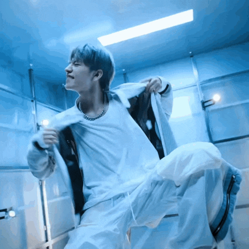 a man in a white shirt and white pants is dancing in a room with blue lights