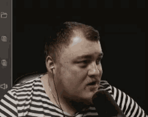 a man wearing ear buds and a striped shirt is speaking into a microphone