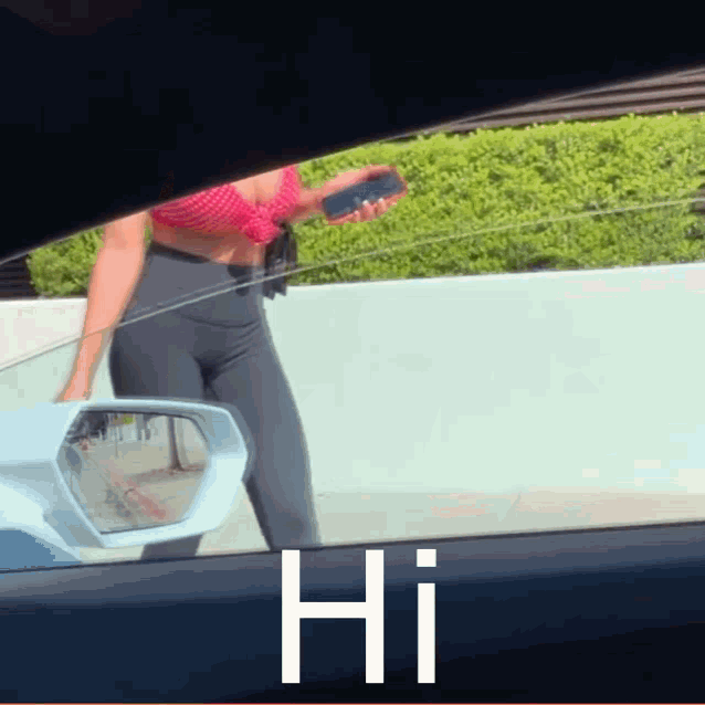 a woman in a red top and black pants is standing in front of a car with the word hi on the side