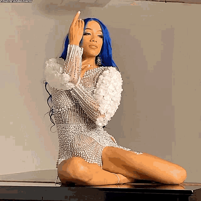 a woman with blue hair is sitting on a piano and making a middle finger sign