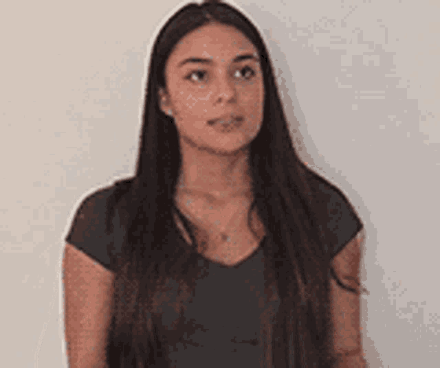 a young woman with long hair is standing in front of a white wall and looking at the camera .
